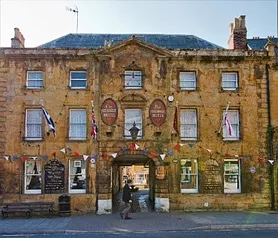 Large Georgian hamstone building with central archway. Originally a coaching inn now a hotel