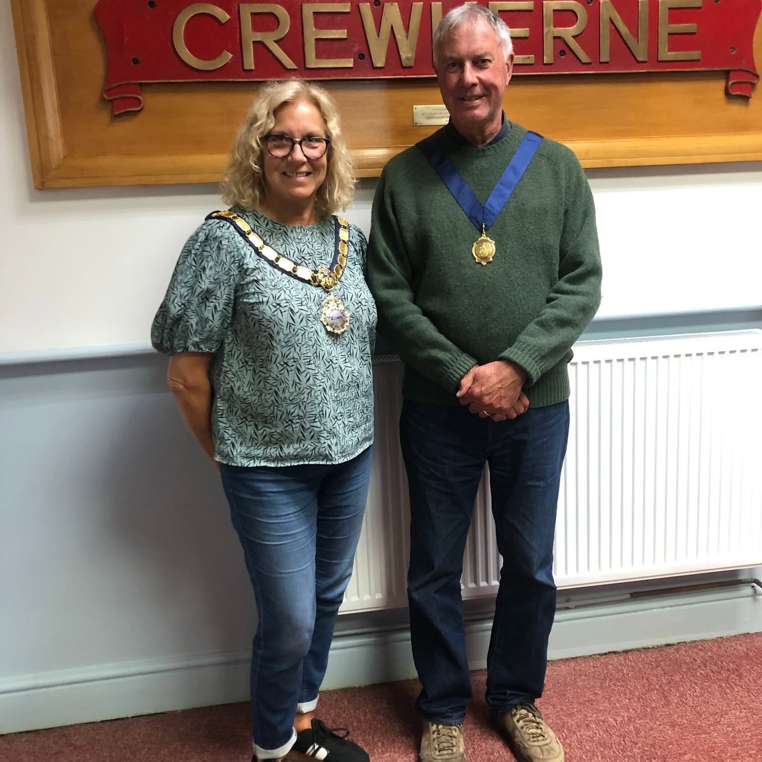An image of Alice Samuel in a green blouse and blue jeans wearing her chain of office. She is stood next to Paul Maxwell in a green jumper and jeans, also wearing his chain.